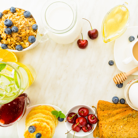 Square shot of overhead healthy breakfast with coffee, detox water, granola on white table with copy space in centerの写真素材