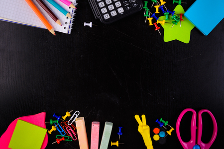 Stationaries (pencils, chalk, pins, scissors, calculator and etc.) on black background with copy space in centerの写真素材