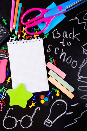 Back to school concept. Stationaries with empty notebook in center with copy space over black table with chalk message. Vertical shotの写真素材