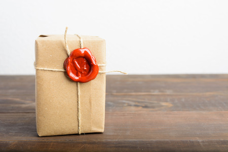 Parcel wrapped in craft paper with rope and red sealing wax over the wooden table with white backgroundの写真素材