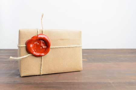 One present in craft paper with red sealing wax over wooden table and wite backgroundの写真素材