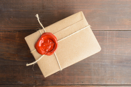 Parcel wrapped in craft paper with rope and red sealing wax over brown wooden table, overhead viewの写真素材