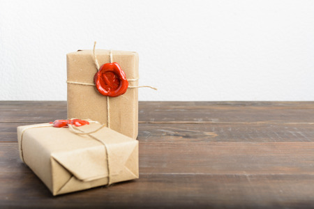 Two gifts wrapped in craft paper with rope and red sealing wax over brown wooden table and white backgroundの写真素材
