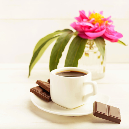 A cup of coffee with chocolate and one flower in vase on white background, toned photo, square shotの写真素材
