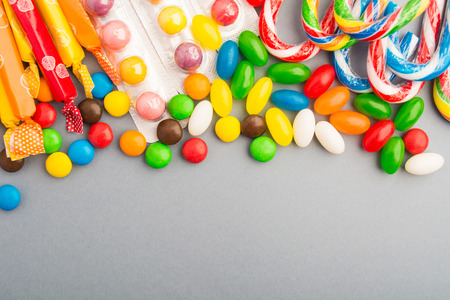 Colorful candies over grey paper background with copy space, overhead view