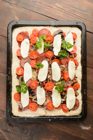 Top view of homemade pizza on baking pan over brown wooden backgroundの写真素材