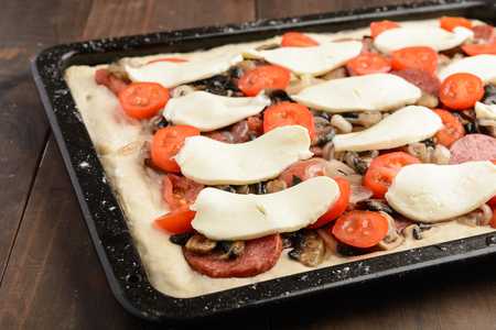Homemade pizza with ingredients ready for baking over brown wooden table, selective focusの写真素材