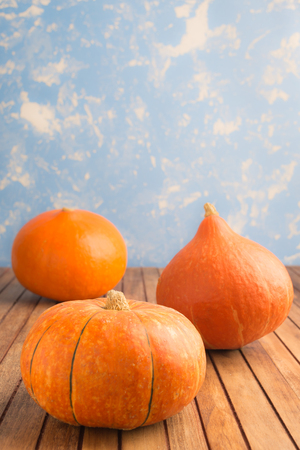 Three pumpkins on blue background on wooden table with copy space, vertical shotの写真素材