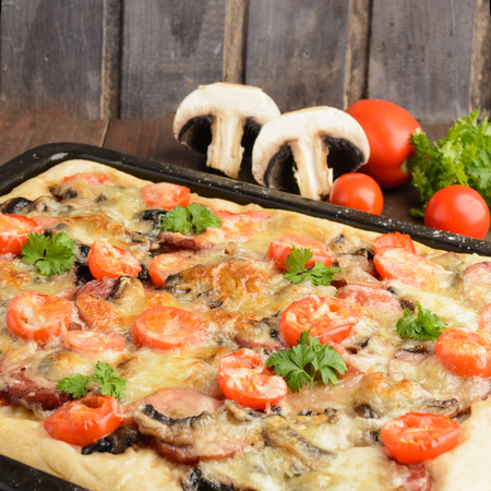 Homemade pizza with tomatoes, mushrooms, sausage and cheese over wooden background, selective focus, square shotの写真素材