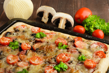 Homemade pizza with tomatoes, mushrooms, sausage and cheese over wooden background, selective focusの写真素材