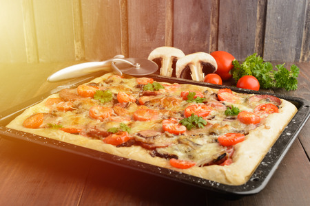 Pizza at home with some ingredients and special knife over wooden background with copy space, toned photoの写真素材
