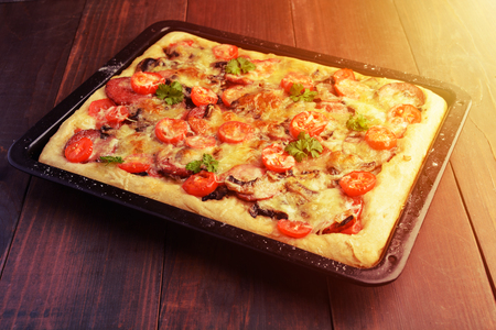 Homemade pizza with tomatoes, mushrooms, sausage and greens on baking pan over wooden background, toned photoの写真素材