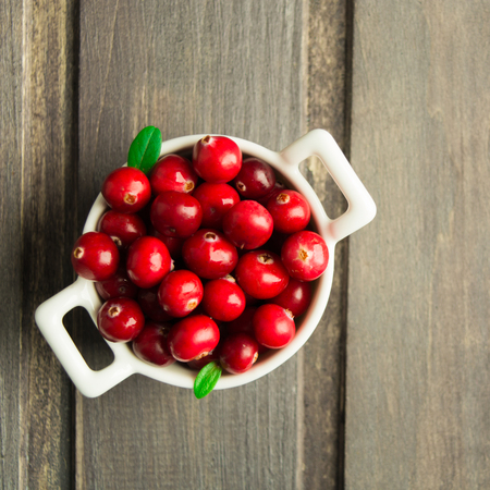 Fresh cranberry in white ceramic bowl on wooden background, overhead view, square shotの写真素材