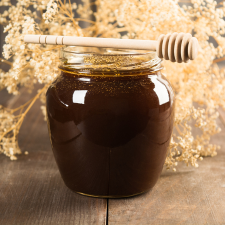 Dark honey with spoon and flowers on background; square shotの写真素材