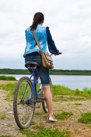Travel woman on bicycle on shore of river looking far away, healthy lifestyle concept, bike travel conceptの写真素材