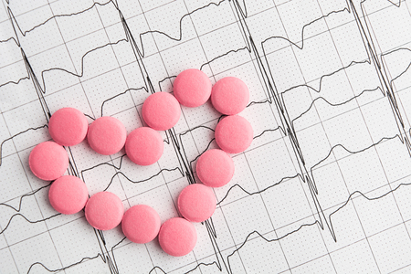 Pills in heart shape over paper cardiogram, overhead view, flat layの写真素材