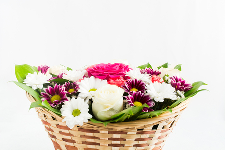 Wicker basket with bouquet of roses, chrysanthemums and camomile with green leaves on white backgroundの写真素材