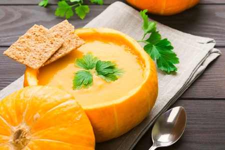 Natural pumpkin with vegetarian pumpkin soup with greens and bread on wooden tableの写真素材