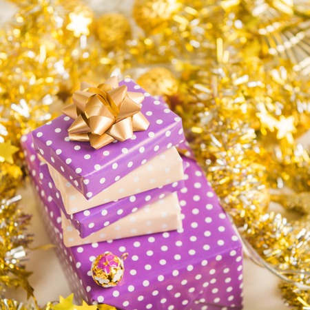 Elegant beige and violet (purple) gift boxes stack with ribbon with golden christmas decoration, New Year presents with golden garland and tinselの写真素材