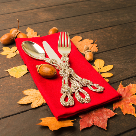 Autumn thanksgiving table with tableware and red tissue over wooden table, square shotの写真素材