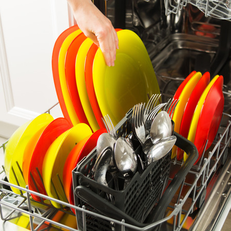 Female hand with clean colorful dish in the open dishwasher, selective focusの写真素材