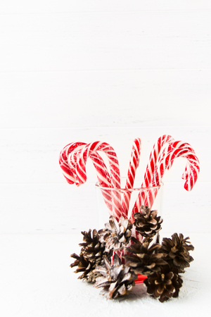 Many red christmas candy canes in glass with pine cones decoration on white background with copy space, vertical shotの写真素材
