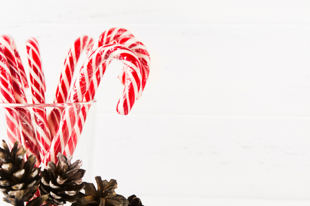 Closeup view of many red christmas candy canes in glass with pine cones decoration on white background with copy spaceの写真素材