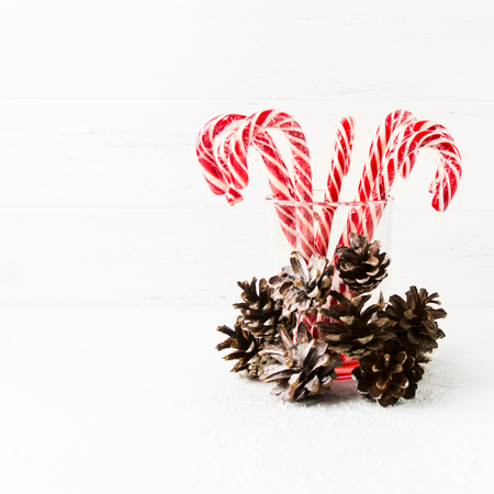 Many red christmas candy canes in glass with pine cones decoration on white background with copy space, square shotの写真素材