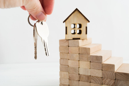 Woman hand hold two keys from house with toy wooden house on stairs with copy spaceの写真素材
