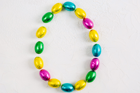 Colorful Easter egg of chocolate candies small eggs on white concrete background, flat lay with copy spaceの写真素材
