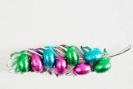 Colorful easter chocolate eggs in shiny wrapping on feather decoration with copy space, flat lay styleの写真素材