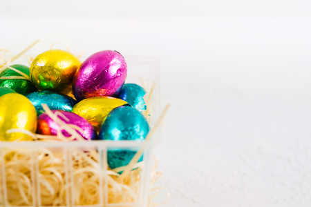 Wrapped chocolate candies with egg's form in plastic basket on white background with copy spaceの写真素材