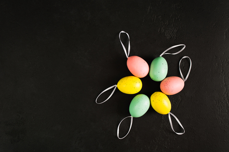 Easter colorful pastel eggs in circle with ribbons over back textured concrete background with copy space. Six fake eggs decoration. Space for text. Flat lay. Top viewの写真素材