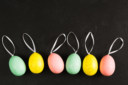 Colorful pastel eggs with ribbons on black background with copy space. Easter card concept with space for text. Flat lay. Top viewの写真素材
