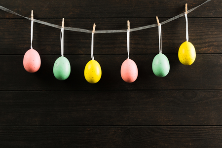 Easter colorful unreal eggs on the rope with wooden background. Dark photo with copy space. Easter concept card with empty space for textの写真素材