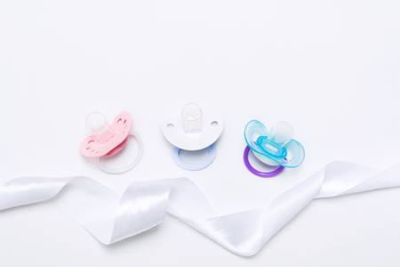 Baby shower with three colorful baby silicone pacifier with holder with ribbon on white background. Mock up. Flat lay. Top view. Orthodontic dummy for babyの写真素材