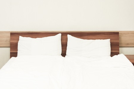 Two white pillows in bed. Minimalism in hotel. Wooden bed. Bed linenの写真素材