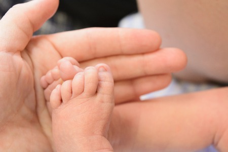 Small cute newborn baby's feet with man's hand. Selective focus