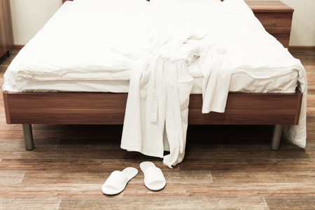 Bed with white linens and white bathrobe with slippers in hotel. Selective focusの写真素材