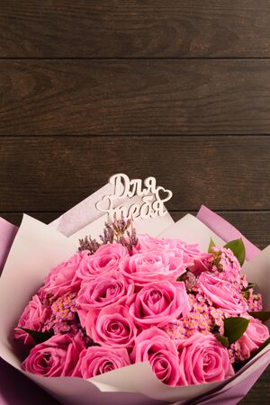 Pink roses in bouquet in colorful paper with wooden text in Russian language on wooden background with copy space. Vertical shotの写真素材