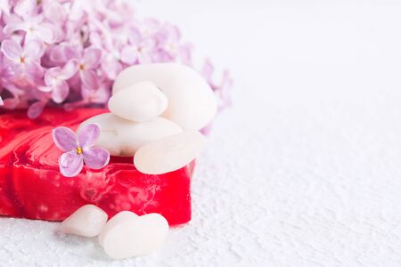 White stones for massage, red soap and lilac flowers for spa concept. Aromatherapy and relaxation. Selective focus. Copy space. Textured white background. Selective focusの写真素材