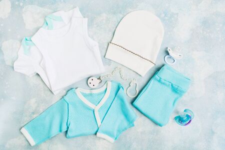 Newborn baby clothes - white bodysuit, blue shirt, blue pants, white hat and pacifiers with holder on blue textured background. Baby shower conceptの写真素材