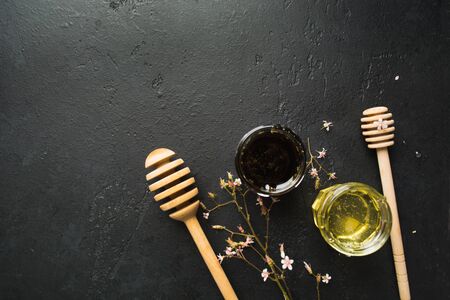 Two type of healthy organic natural honey with spoons and small flowers on black stone background with copy space. Top view. Spa ingredient and medicine conceptの写真素材