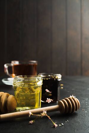 Dark and light hone in glass jars with wooden stick on black stone and wooden background with copy space. Healthy organic natural food for treatment for colds. Vertical shotの写真素材