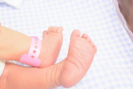 Two baby feet with special tag from maternity hospital. Selective focus. Blue nappy backgroundの写真素材