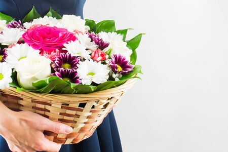 Woman in blue dress holding flowers in wicker basket in hands. White background. Copy spaceの写真素材
