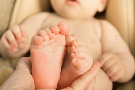 Small cute baby feet in female hand with part of baby on backgroundの写真素材