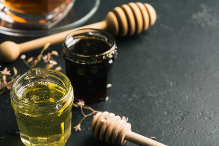 Dark and light honey in glass jars with wooden sticks on black stone background with copy space. Healthy organic natural food for treatment for colds. Spa conceptの写真素材