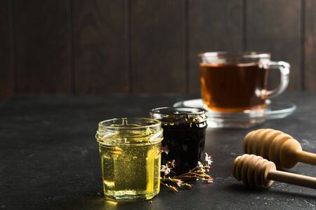 Healthy organic natural food for treatment for colds. Dark and light honey in glass jars with wooden sticks on black stone background. Spa concept. Copy spaceの写真素材
