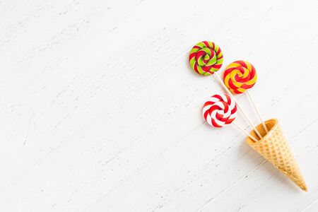 Waffle cone with round colorful lollipops on sticks. Colorful sweets over white wooden background with copy space. Flat lay top viewの写真素材